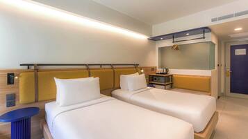 A hotel room with two beds, a small table, a mirror, and a door.