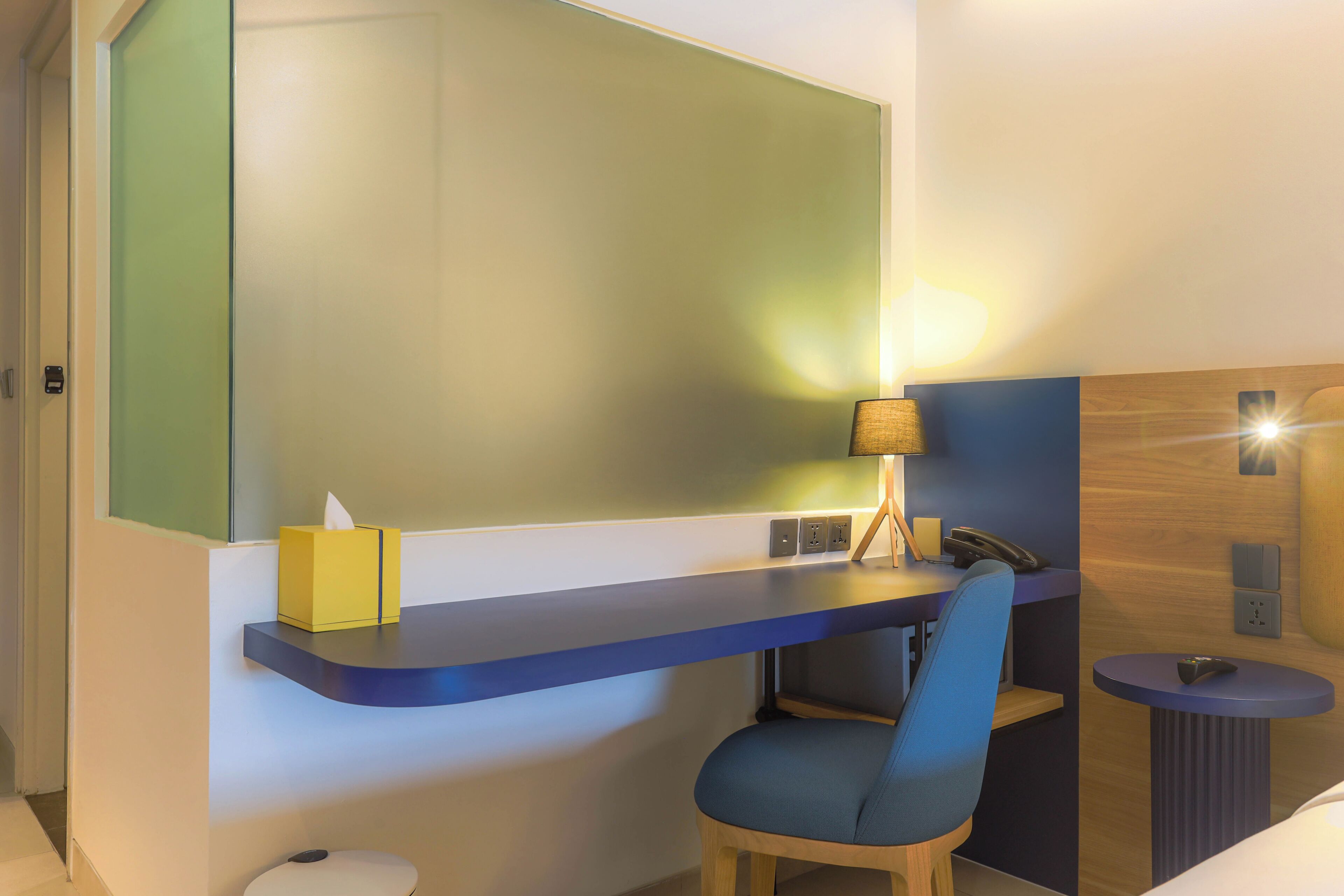 Una habitación de hotel con escritorio, silla, mesita de noche, lámpara y espejo.