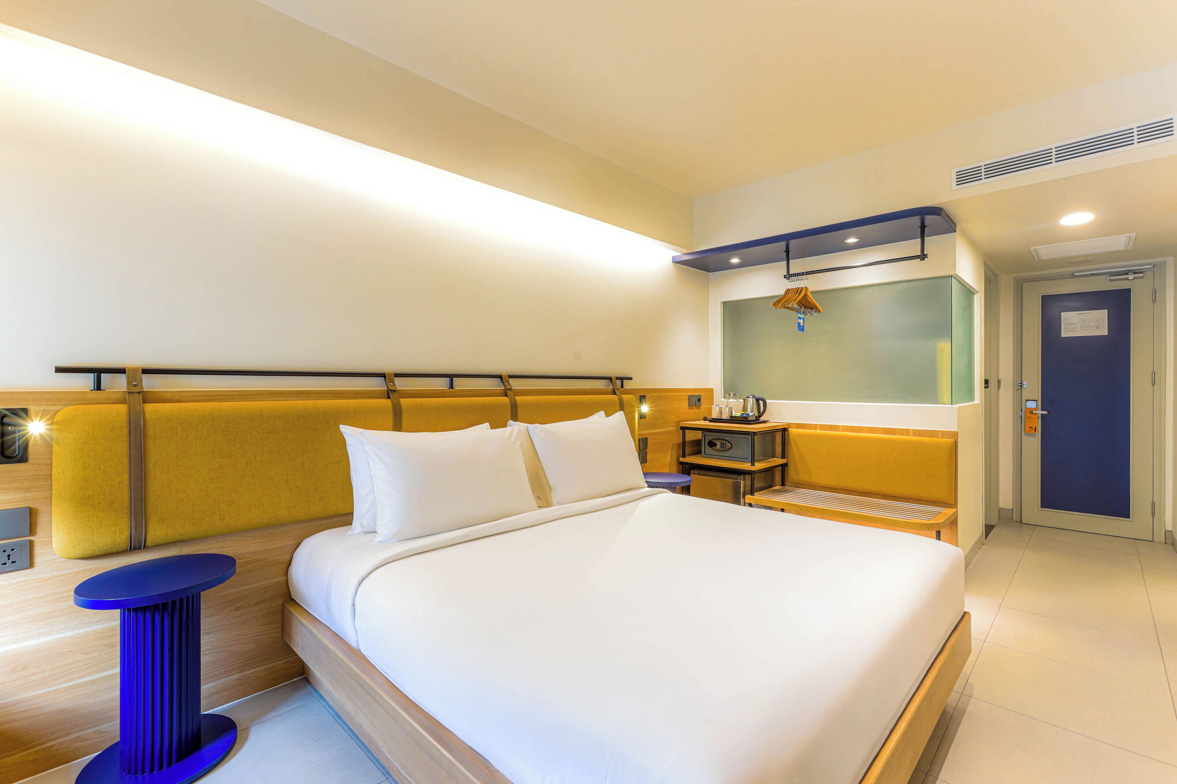 Quarto de hotel com uma cama grande, mesas de cabeceira, um espelho e uma porta.