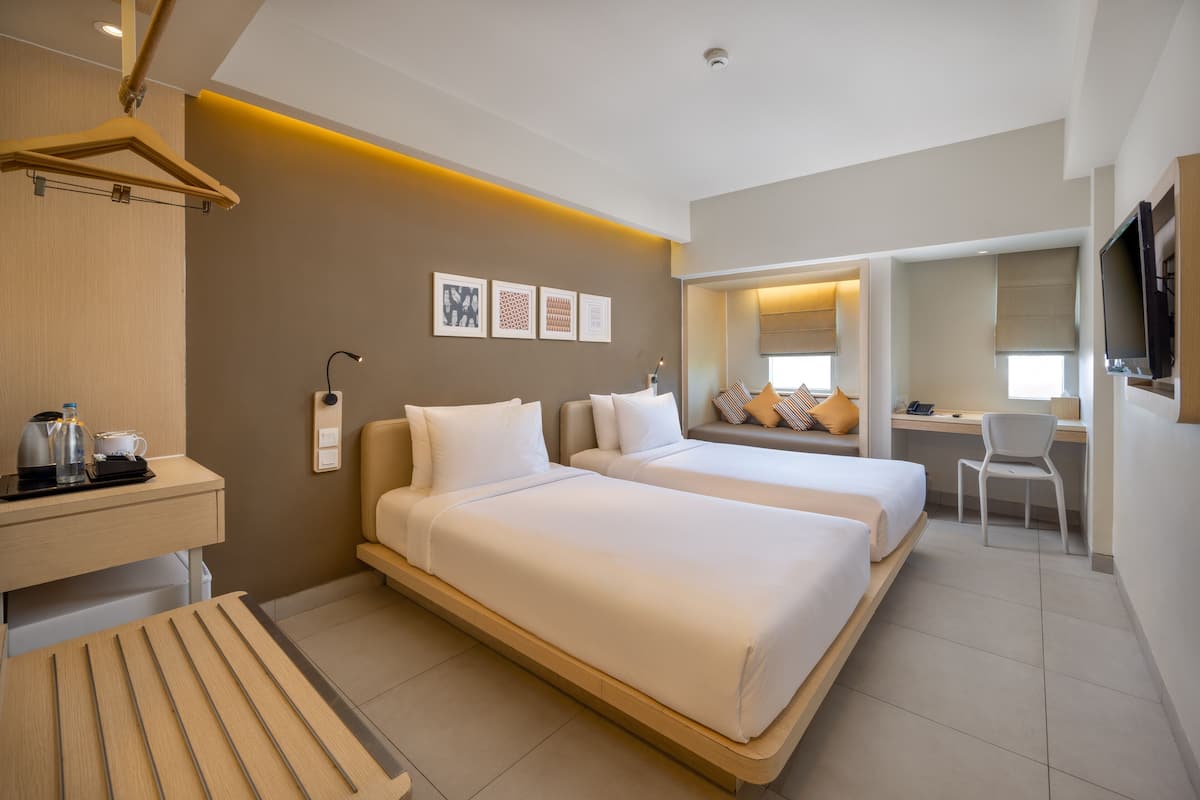 A hotel room with two beds, a desk, a chair, a TV, and a coffee station.