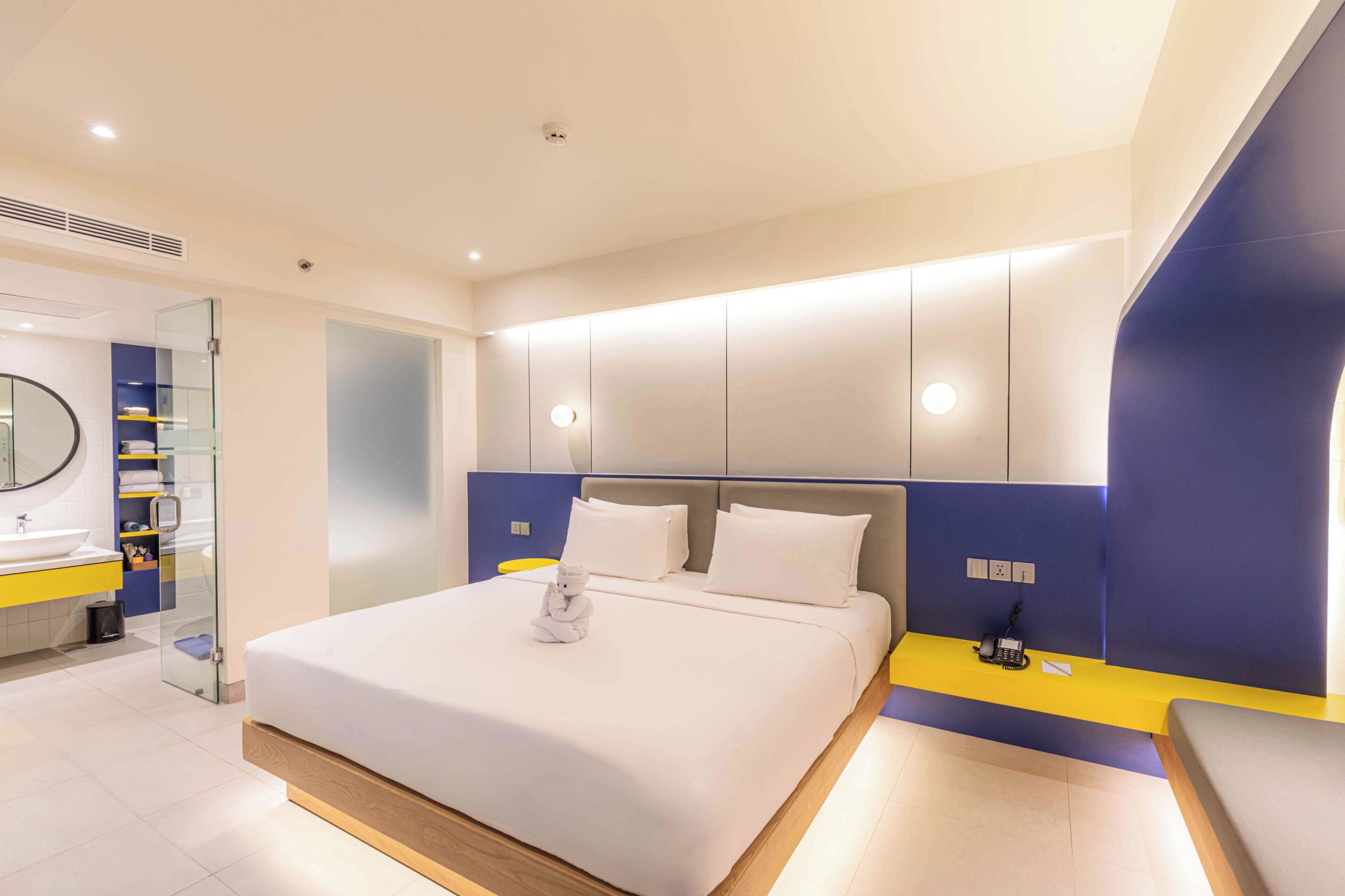 Una habitación de hotel moderna con una cama grande, una mesita de noche con un teléfono y una cabina de ducha de vidrio.