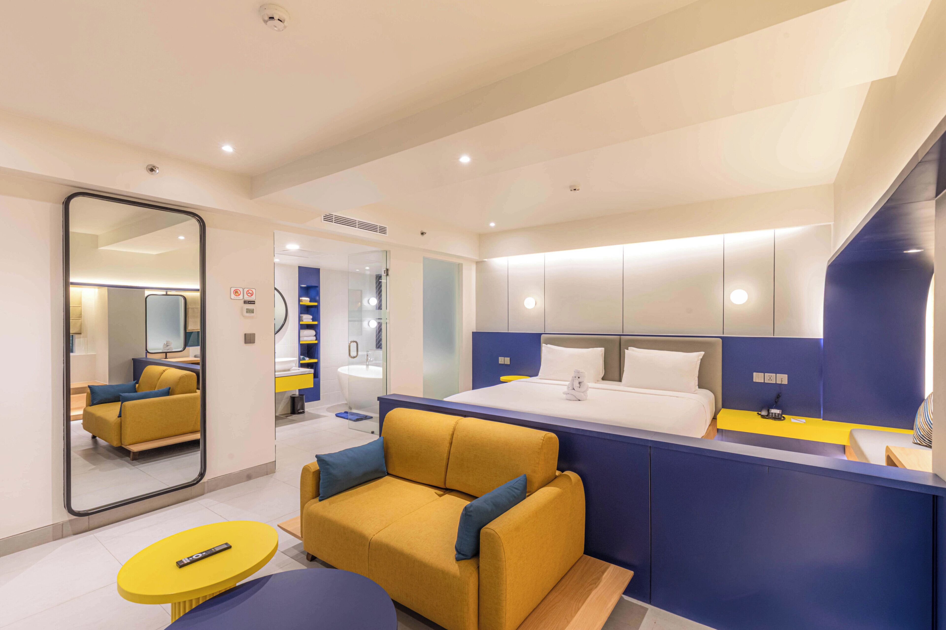 A modern hotel room with a bed, a sofa, a small table, and a mirror.