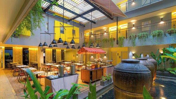 A spacious indoor area with tables and chairs, a water feature, and hanging plants. - Sevn Legian (Legian)