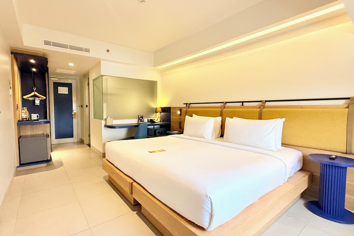 A hotel room with a bed, bedside table, lamp, and a mirror.