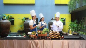 A group of chefs preparing food in an outdoor setting with a yellow and blue building in the background. - Sevn Legian (Legian)