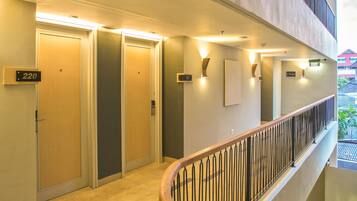 A hotel corridor with doors numbered 220, 221, and 222, a staircase with a wooden handrail, and a balcony with a metal railing.