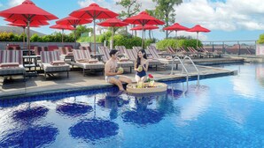 A pool area with lounge chairs and red umbrellas, a poolside bar, and a clear view of the sky. - Sevn Legian (Legian)