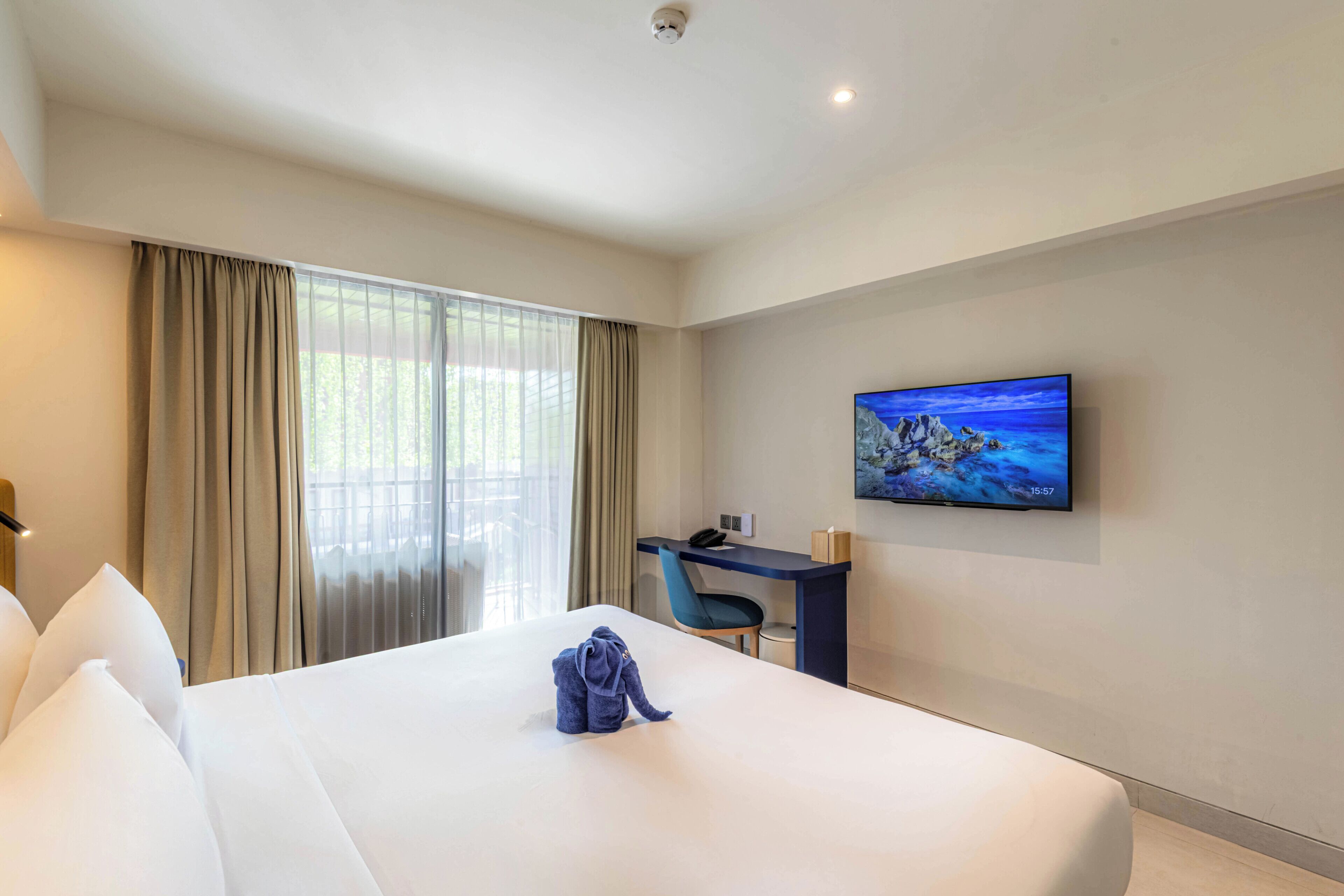 A hotel room with a bed, a desk, a chair, a TV, and a window with curtains.