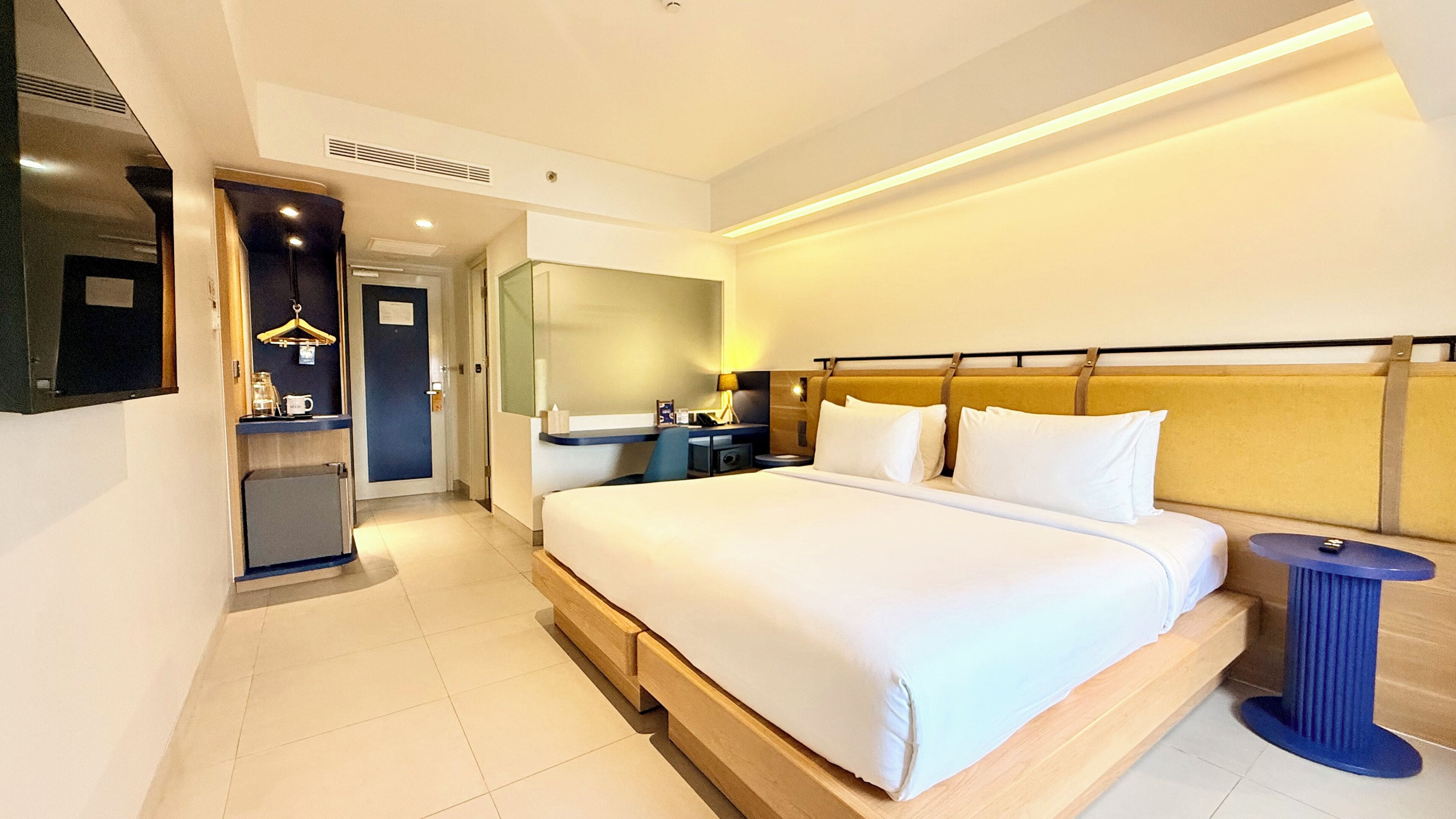 A hotel room with a large bed, bedside table, and a mirror.