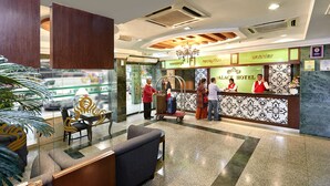 A hotel reception area with a concierge desk, a reception counter, and a seating area with a table and chairs. - Palace Hotel (Kuala Lumpur)
