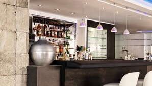 Un'area bar moderna con diverse bottiglie di liquori, un'ampia composizione floreale e luci a sospensione.