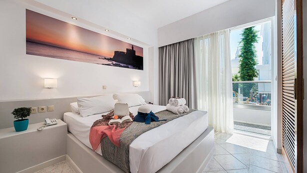 Una camera d'albergo moderna con un letto grande, un dipinto raffigurante un tramonto, un balcone con tende e una piccola pianta sul comodino.