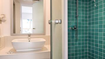 A bathroom with a white sink, a mirror, and a shower with green tiles.