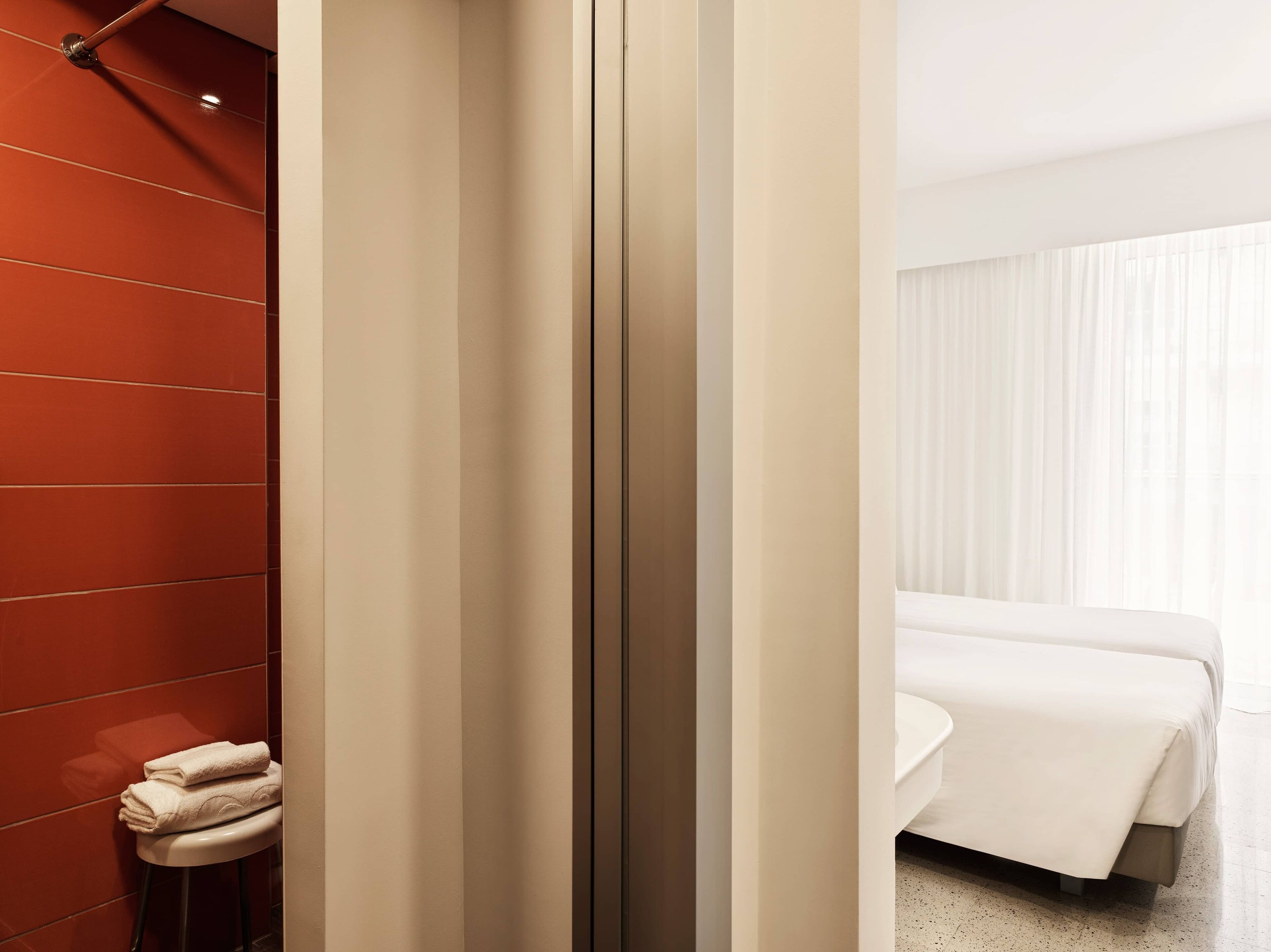 A modern bathroom with a red tiled wall, a white toilet, and a white sink.