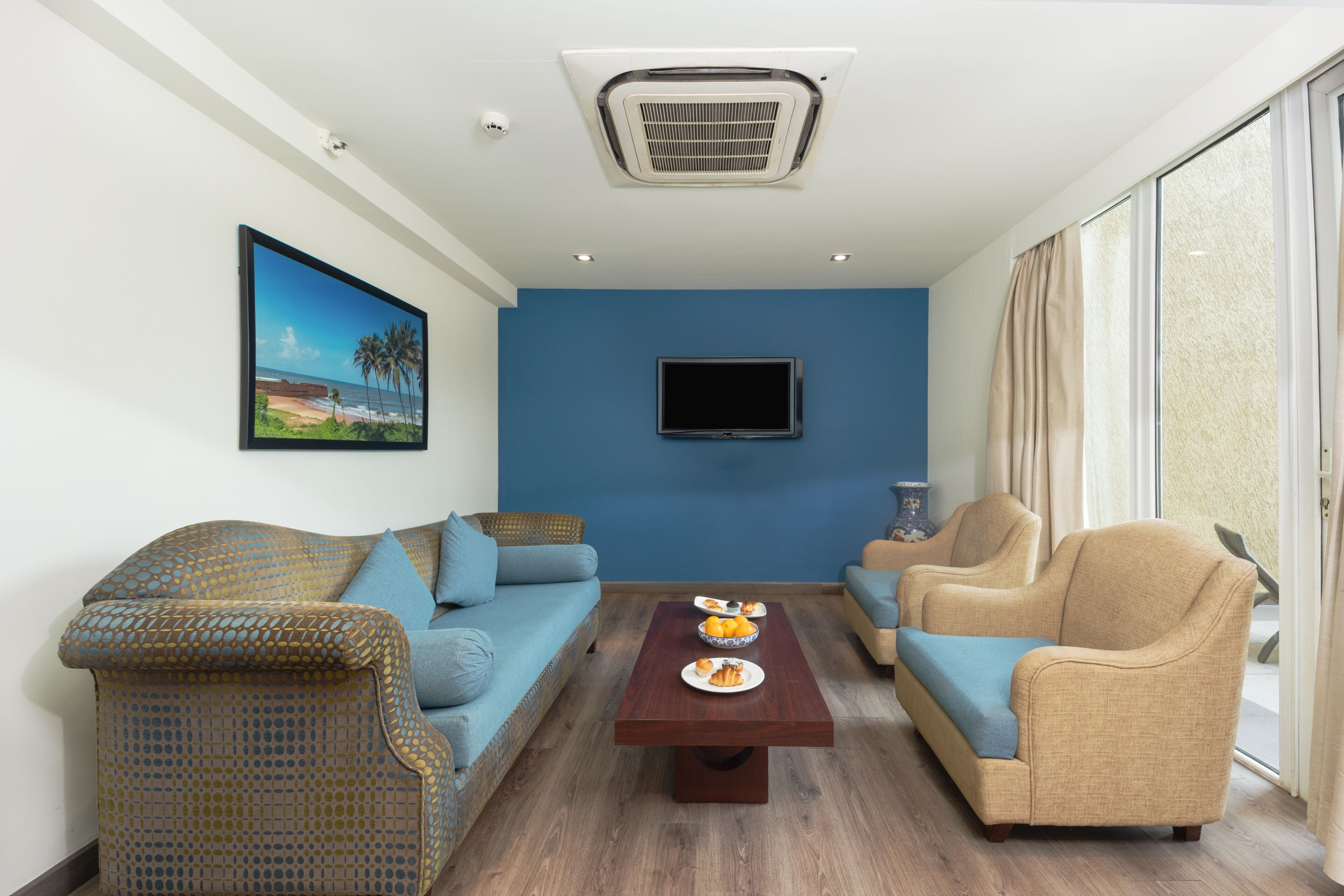 Una sala de estar con pared azul, un televisor de pantalla plana, una mesa de centro de madera con platos de comida y dos sofás.