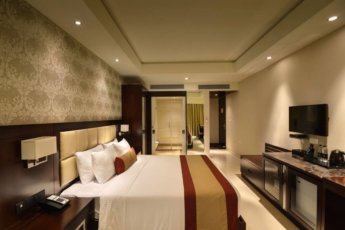 Ein Hotelzimmer mit einem großen Bett, einem Fernseher, einem Schreibtisch und einem durch eine offene Tür einsehbaren Badezimmer.