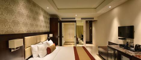A hotel room with a large bed, a TV, a desk, and a bathroom visible through an open door.