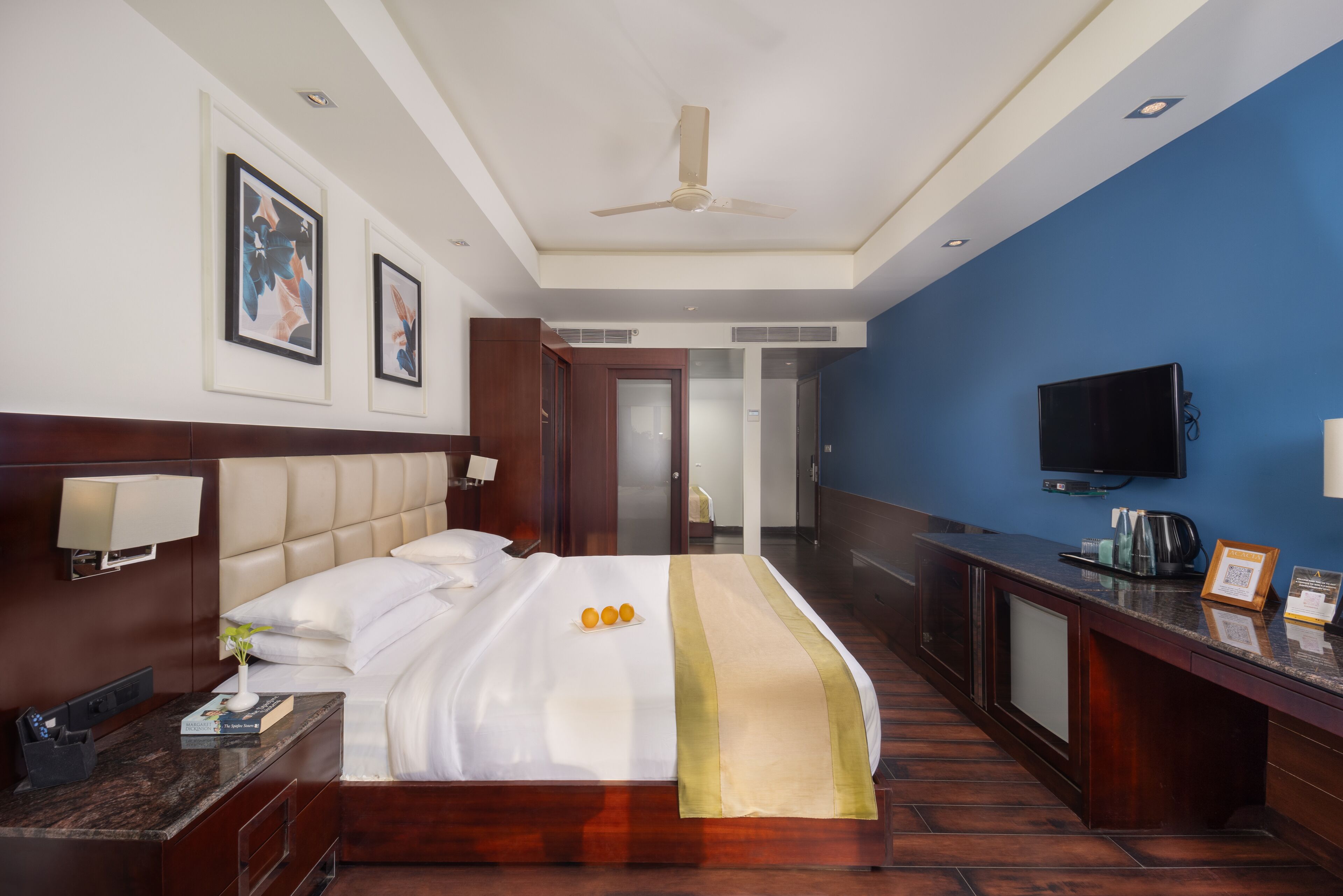 Hotelkamer met een groot bed, een bureau met een flatscreen-tv, een plafondventilator en kunstwerken aan de muur.