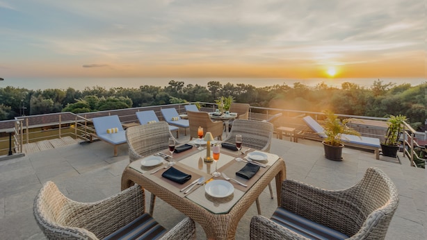 Una terraza en la azotea con mobiliario de mimbre, una mesa dispuesta para comer y vistas al atardecer.