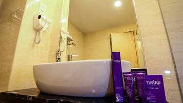 A bathroom with a white sink, a hairdryer mounted on the wall, and toiletries on the counter.