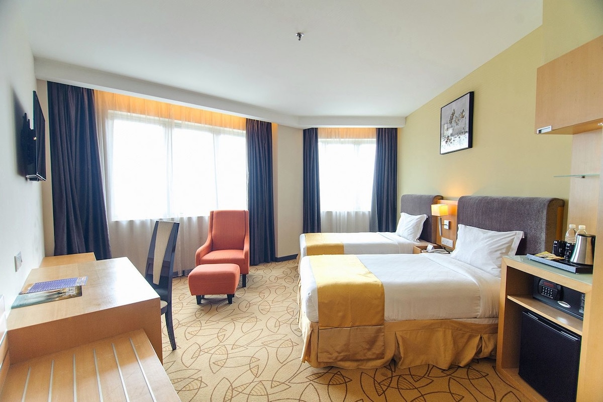 A hotel room with two beds, a desk, a chair, a TV, and a minibar.