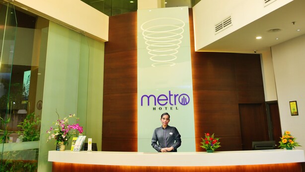 A hotel reception area with a modern design, featuring a central reception desk, a large illuminated circular light fixture, and a visible logo. - Metro Hotel (Kuala Lumpur)