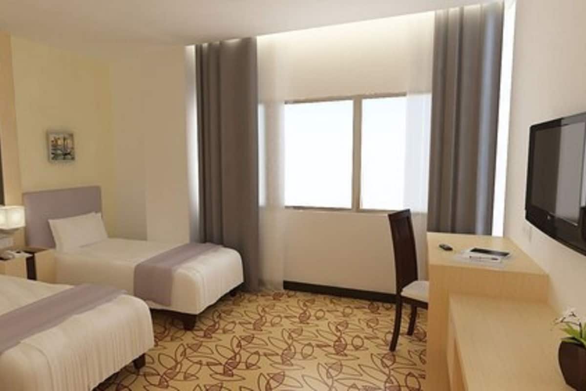 A hotel room with two beds, a desk, a TV, and a window with curtains.