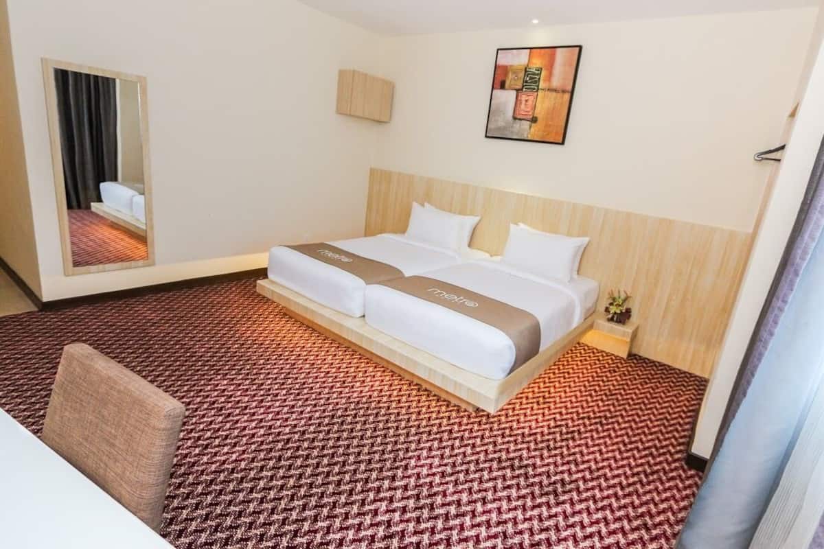 A hotel room with a large bed, a mirror, a small bedside table with a lamp, and a carpeted floor.