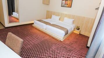 A hotel room with a large bed, a mirror, a small bedside table with a lamp, and a carpeted floor.