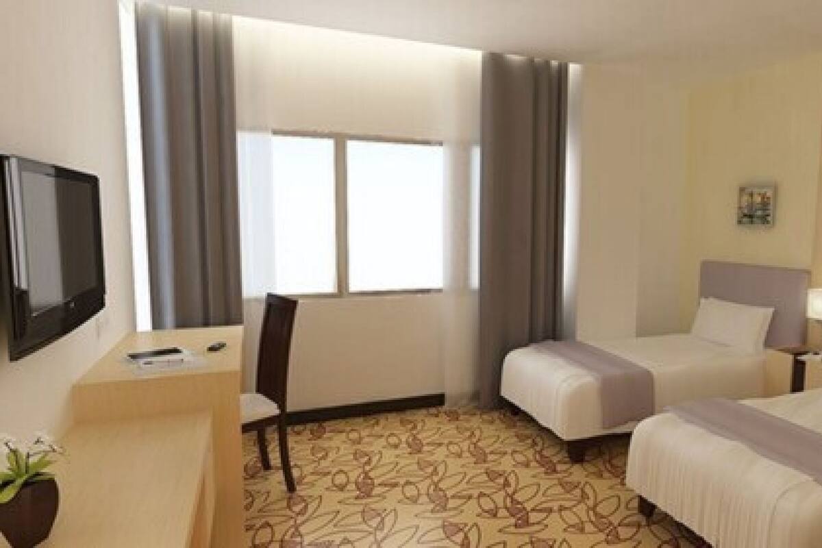 A hotel room with two beds, a desk with a TV, and a window with curtains.