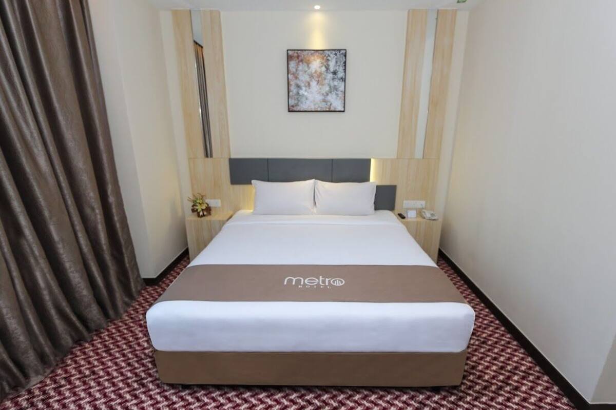 A hotel room with a large bed, a headboard, bedside tables, a nightstand, a lamp, and a painting on the wall.