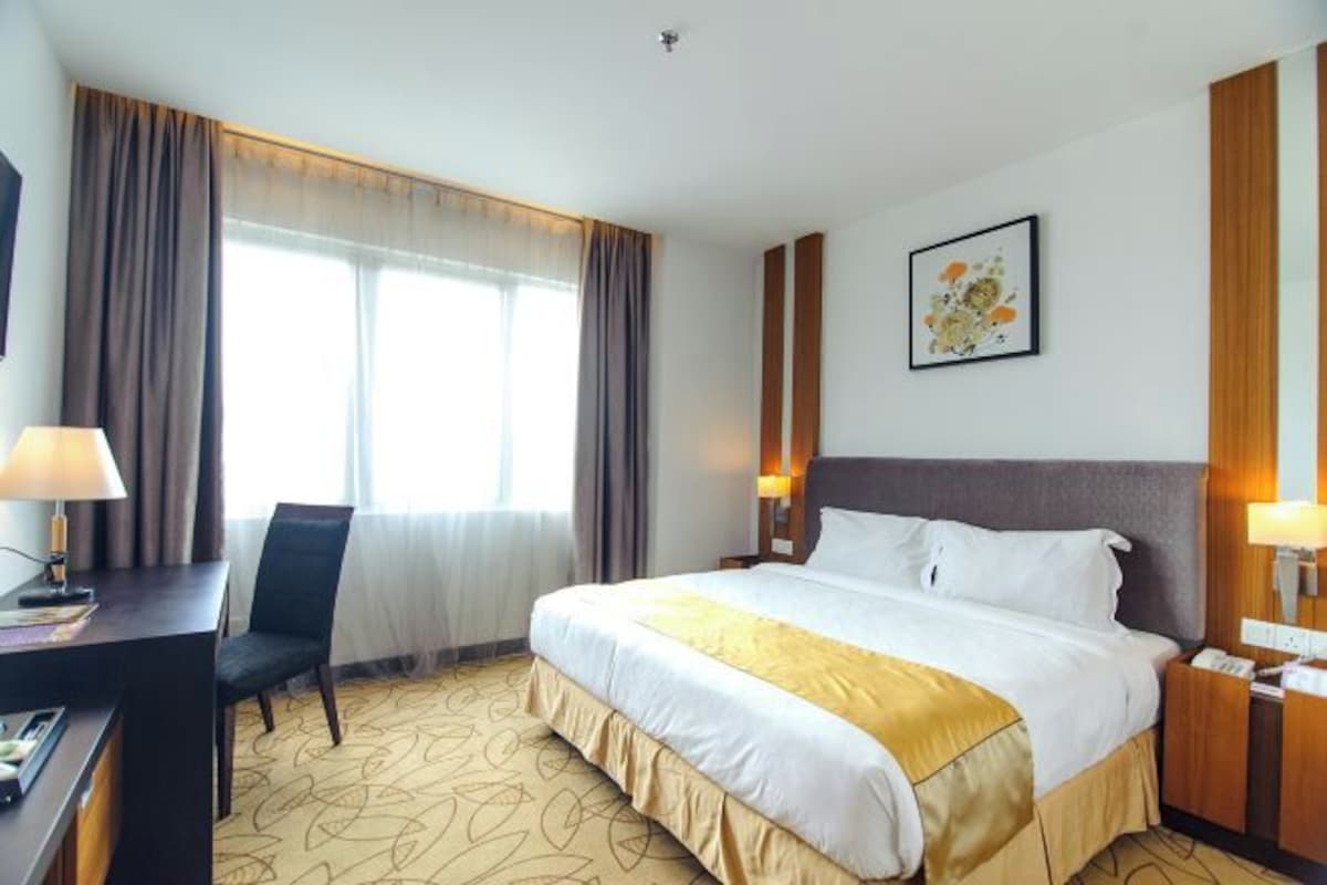 A hotel room with a large bed, a desk with a lamp, a chair, and a bedside table with a phone.