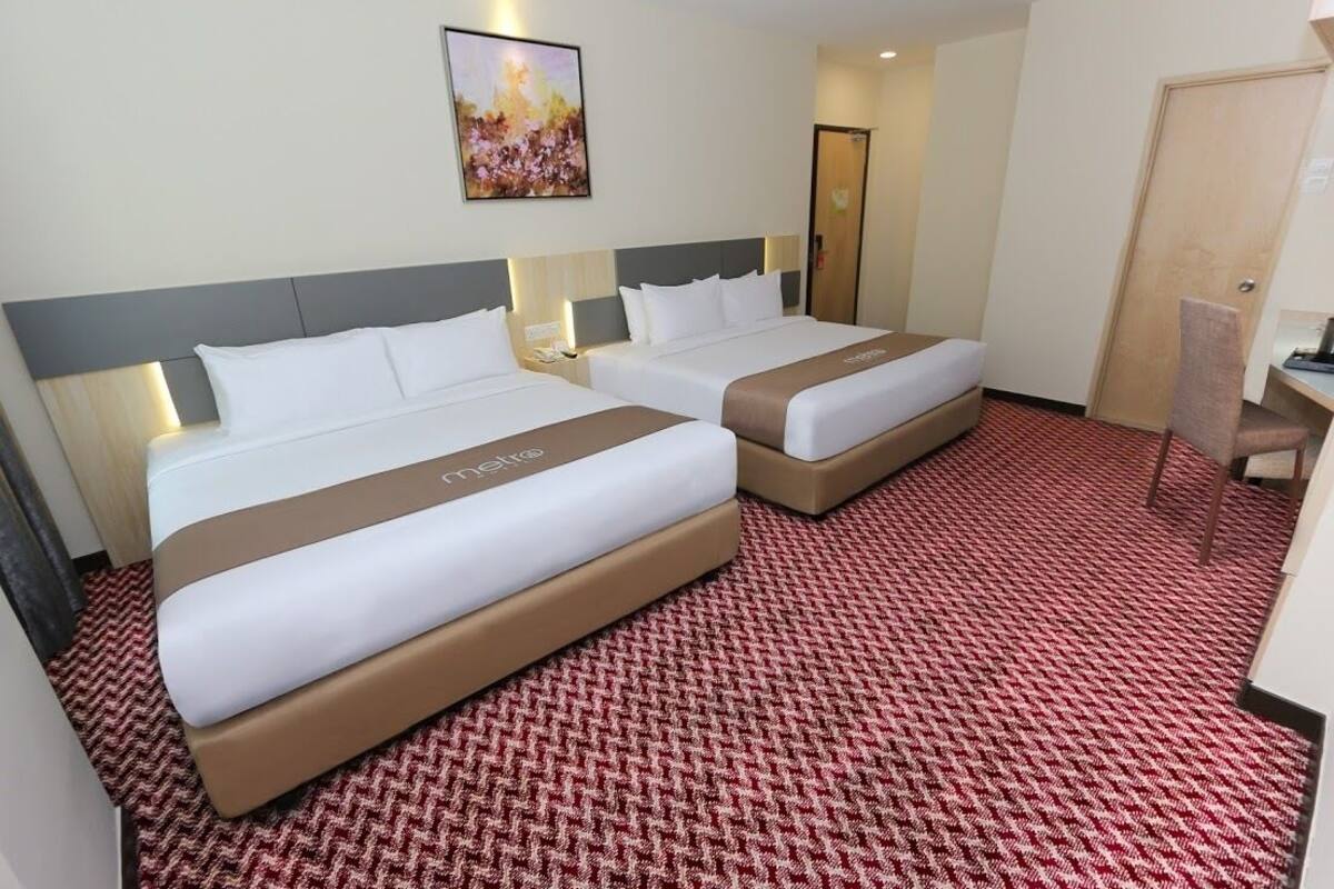 A hotel room with two beds, a red and white patterned carpet, and a painting on the wall.