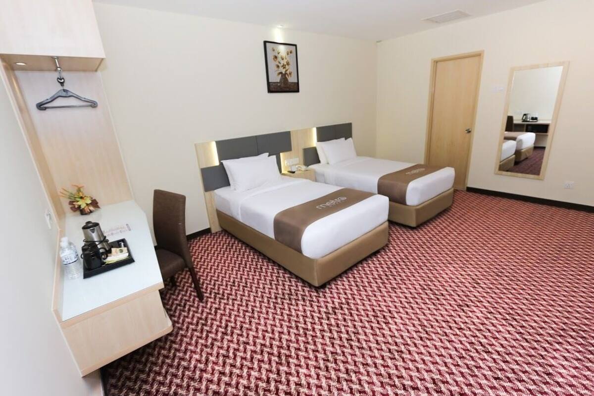 A hotel room with two beds, a desk with a chair, a small table with a coffee maker, and a mirror on the wall.