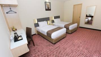 A hotel room with two beds, a desk with a chair, a coat rack, and a mirror on the wall.