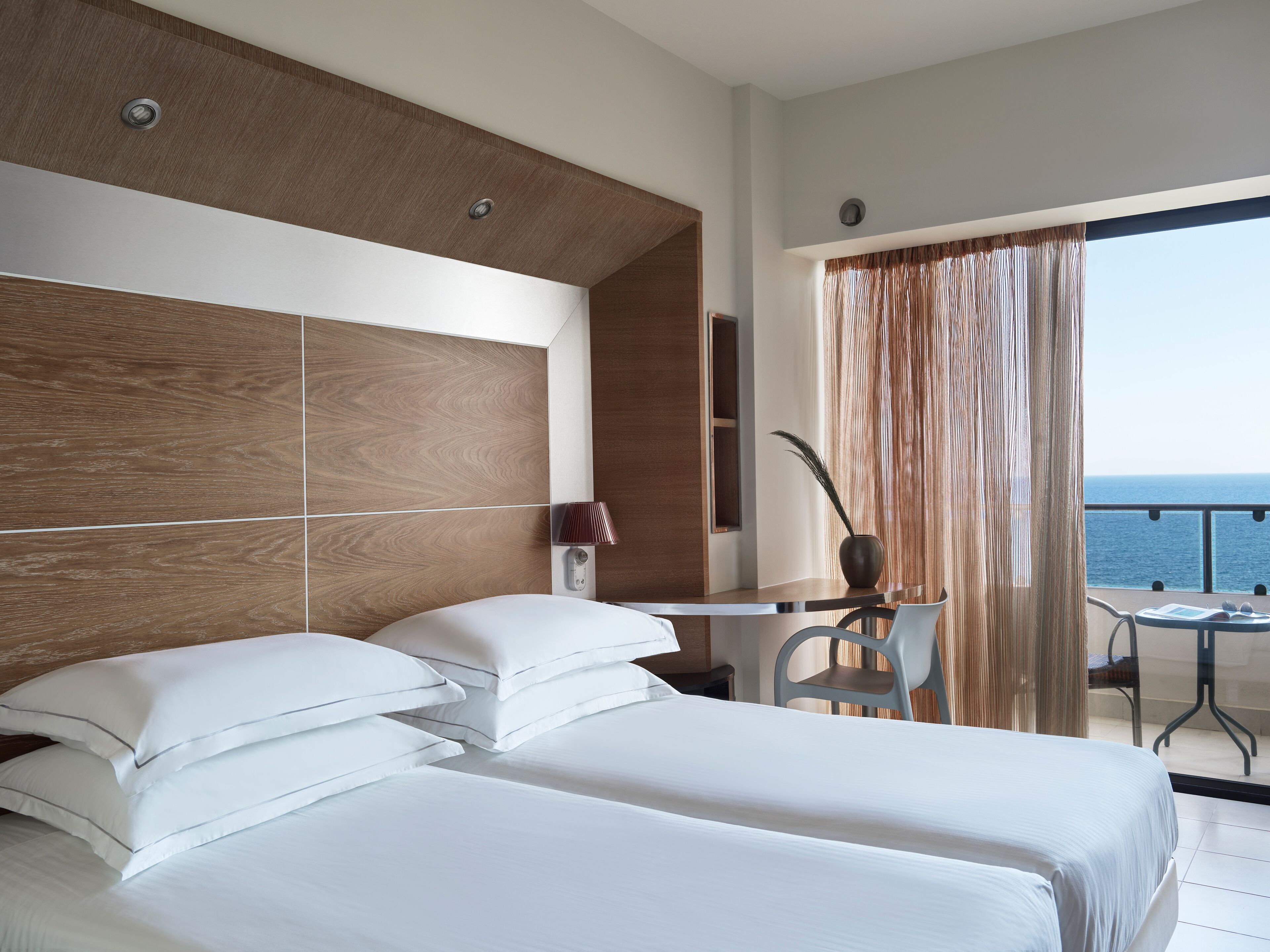A modern hotel room with a large bed, a desk, and a view of the sea.