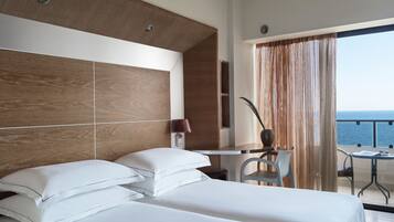 A modern hotel room with a large bed, a desk, and a view of the sea.