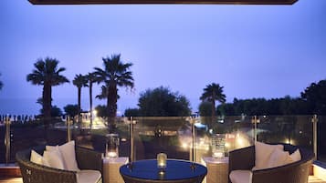 Zona de estar exterior con mobiliario de mimbre y balaustrada de cristal con vistas a la playa.