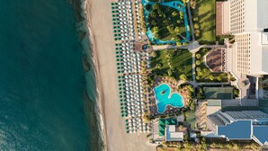 Vista aérea de un complejo turístico con varias piscinas, una zona de playa y un amplio estacionamiento.