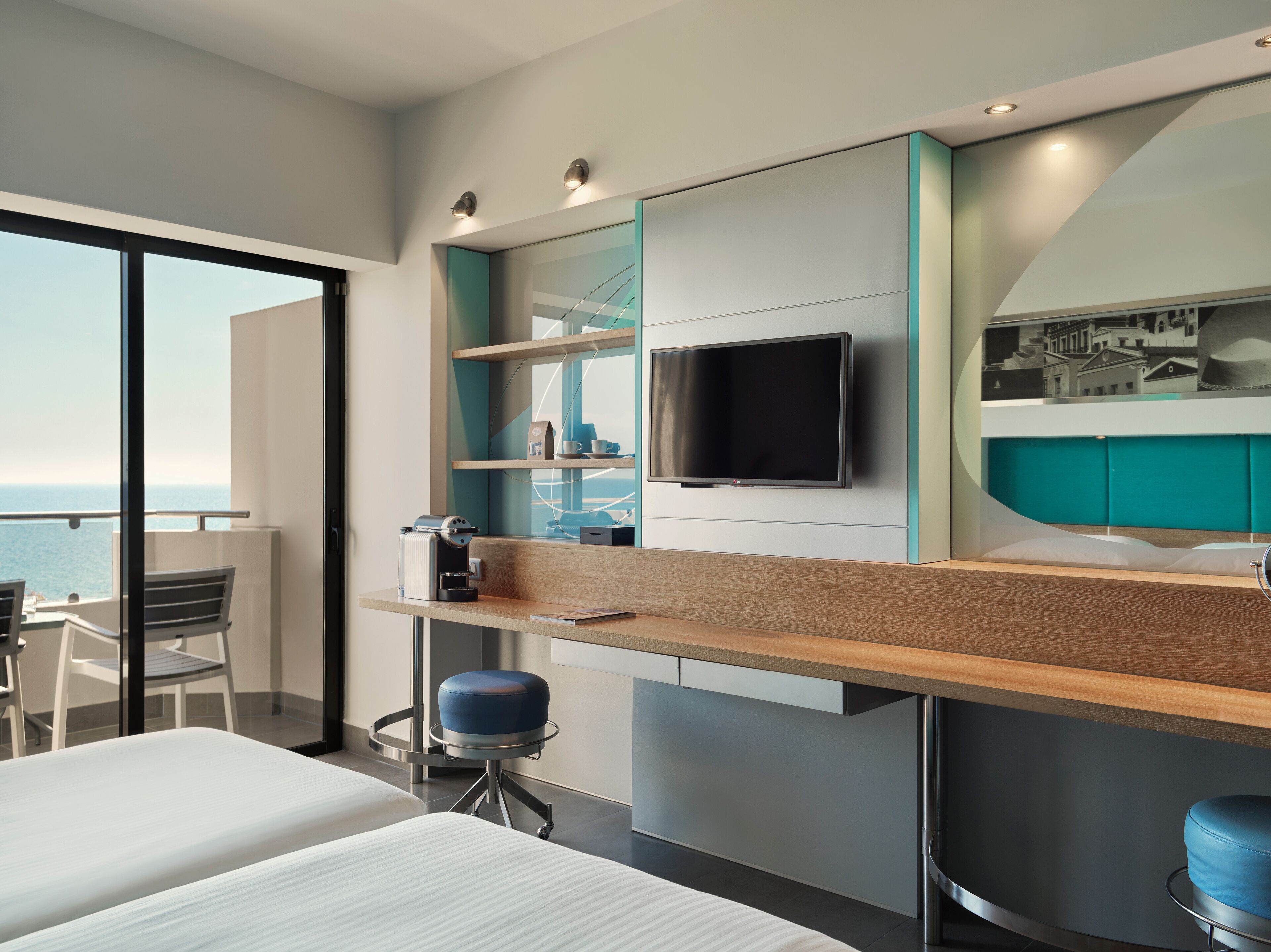 Ein modernes Hotelzimmer mit Balkon, Flachbildfernseher, Kaffeemaschine und einer kleinen Sitzecke.
