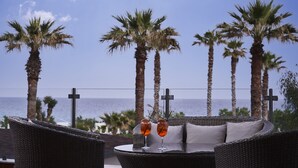 Una silla lounge de mimbre con dos vasos de una bebida, con vista al mar y palmeras.