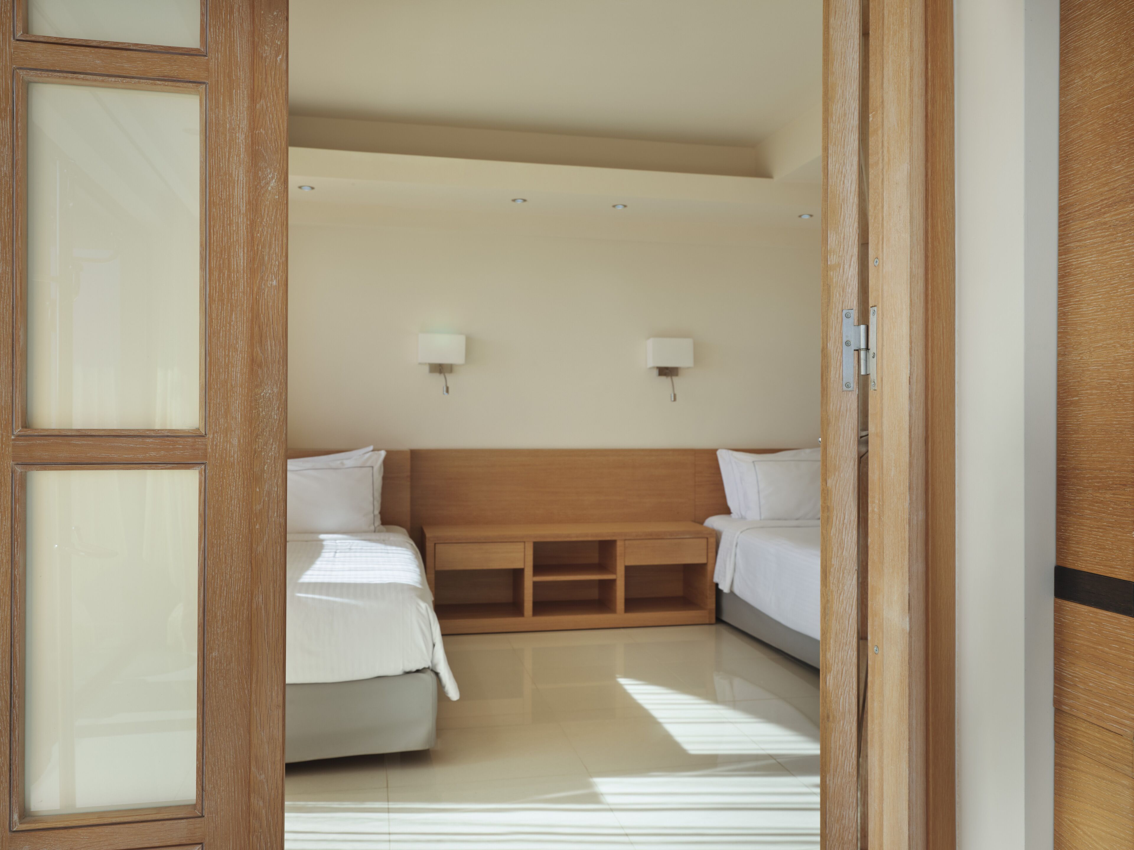 A hotel room with two beds, a wooden headboard, and two wall-mounted lamps.