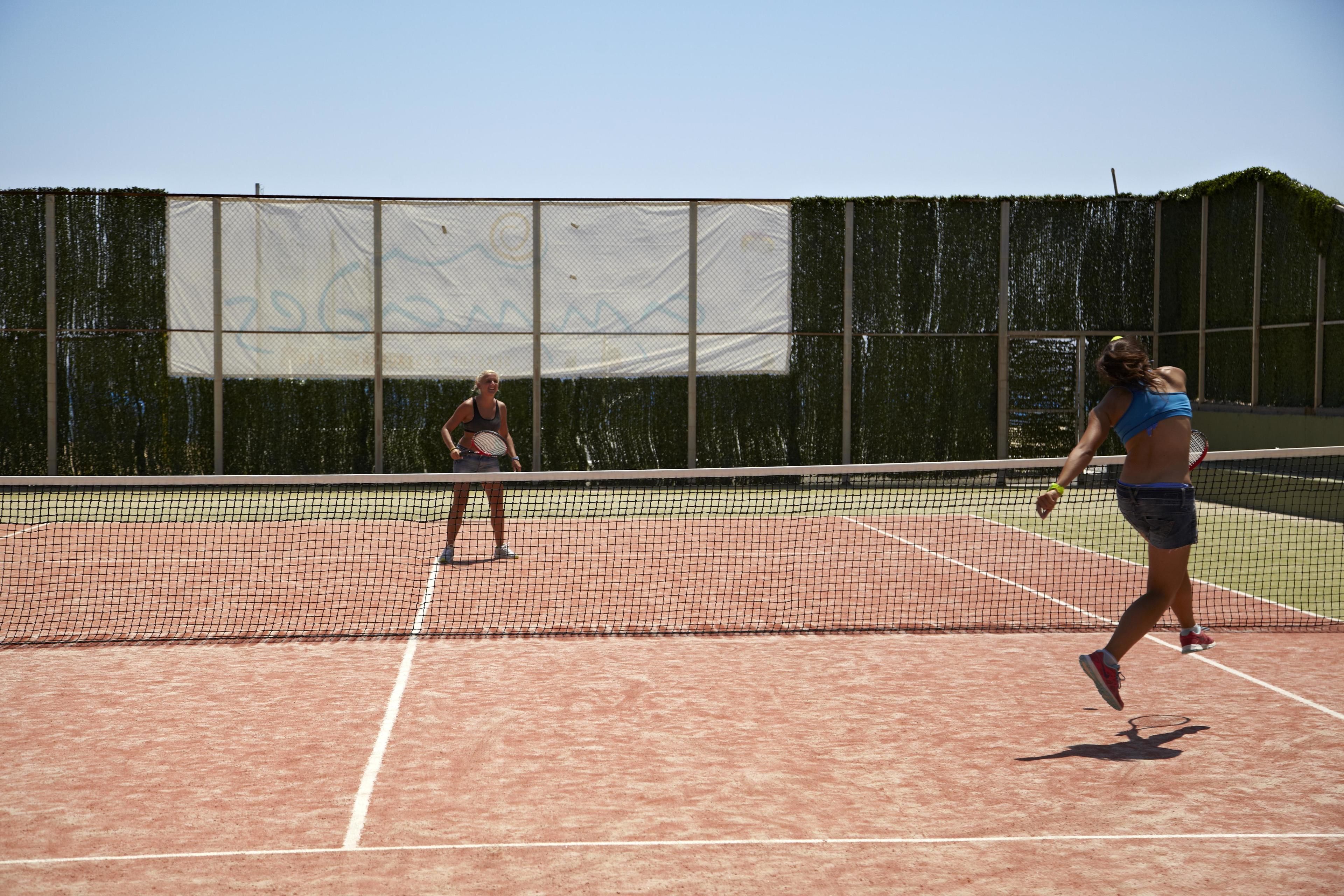 Una cancha de tenis con una red en el centro, rodeada por una valla.