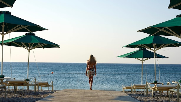 A woman walking on a wooden pier towards the sea, with beach umbrellas and lounge chairs on either side. - Esperos Mare Resort & Spa (Rhodes)
