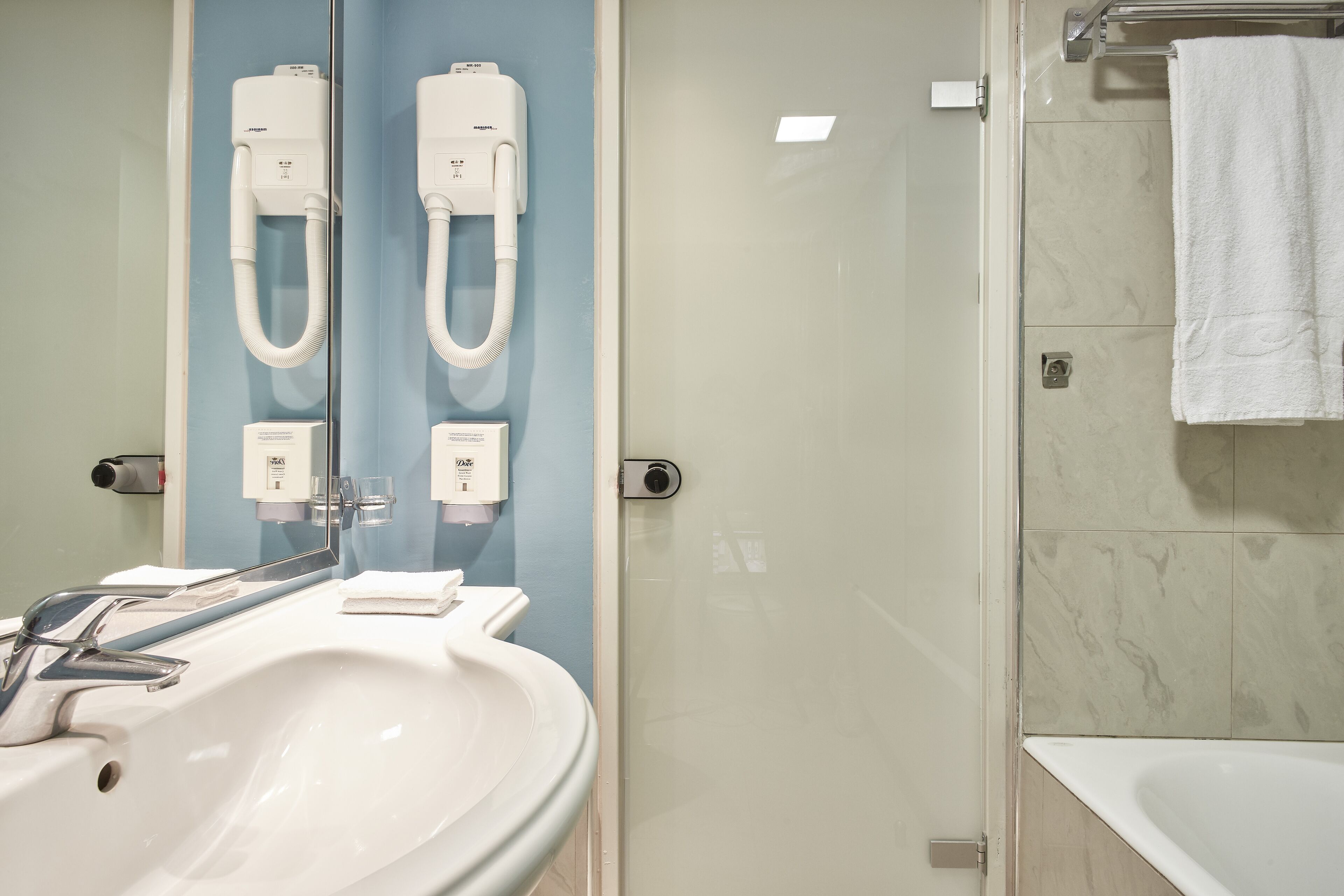 A bathroom with a white sink, two hand dryers, and a glass shower enclosure.