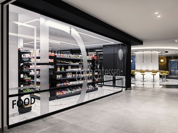 Une épicerie moderne avec une façade en verre, des étagères remplies de divers produits et un espace détente avec des chaises jaunes.