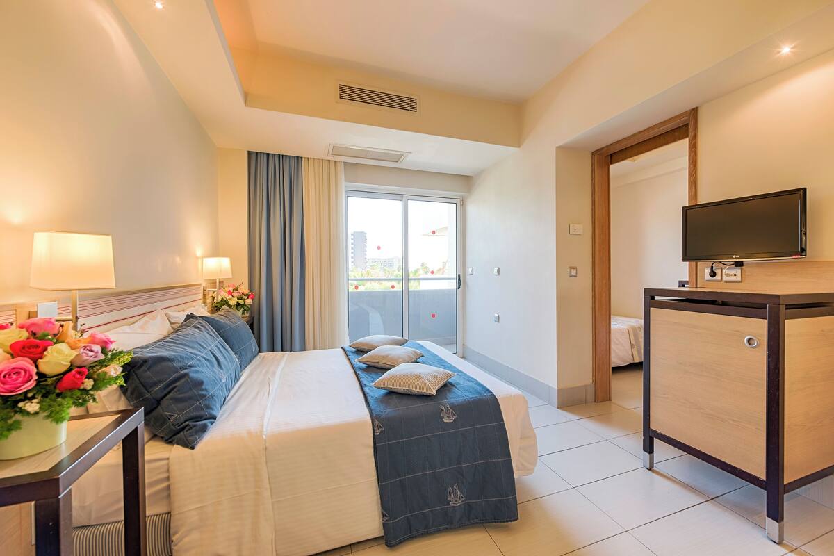 A hotel room with a bed, bedside lamps, a desk with a lamp, a TV, and a view of the outdoors.