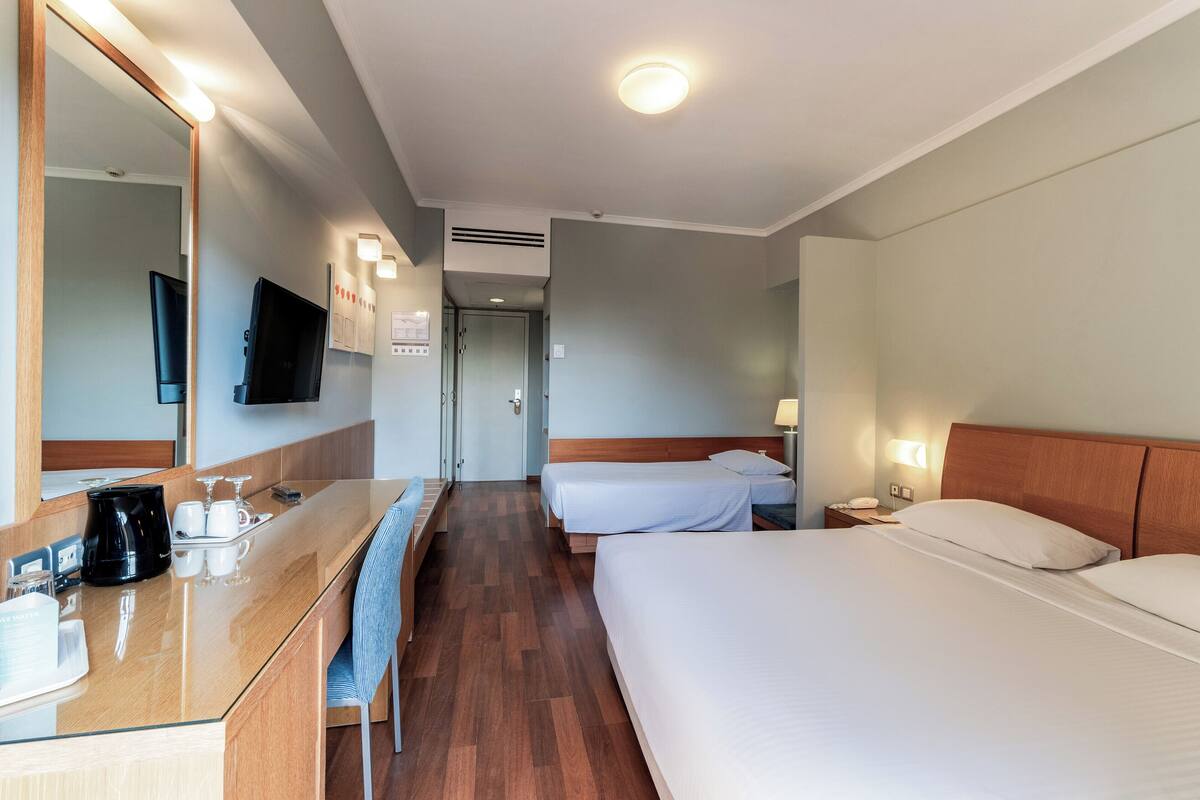 A hotel room with a wooden desk, two beds, a TV, and a mirror.