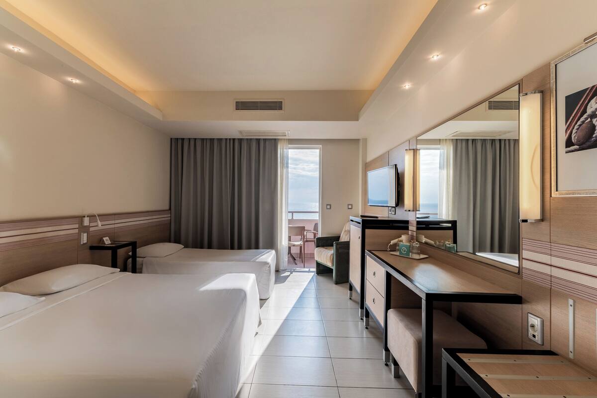 A hotel room with two beds, a desk, a chair, a TV, and a large mirror.