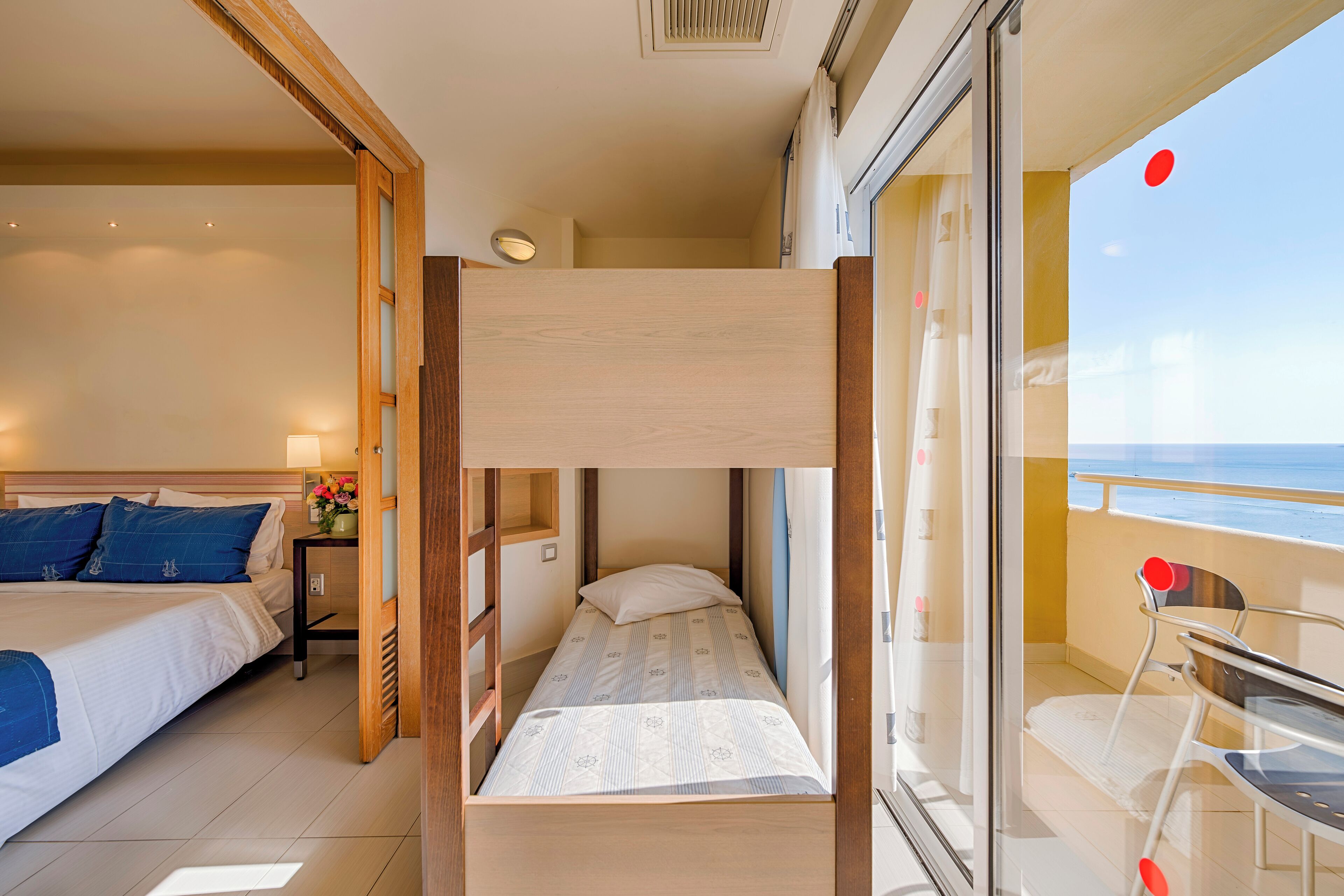 Una habitación con literas, una cama individual, una mesita con silla y un balcón con vista al mar.